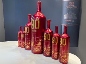 Eine Reihe roter Weinflaschen mit goldener „90“-Aufschrift in verschiedenen Größen.